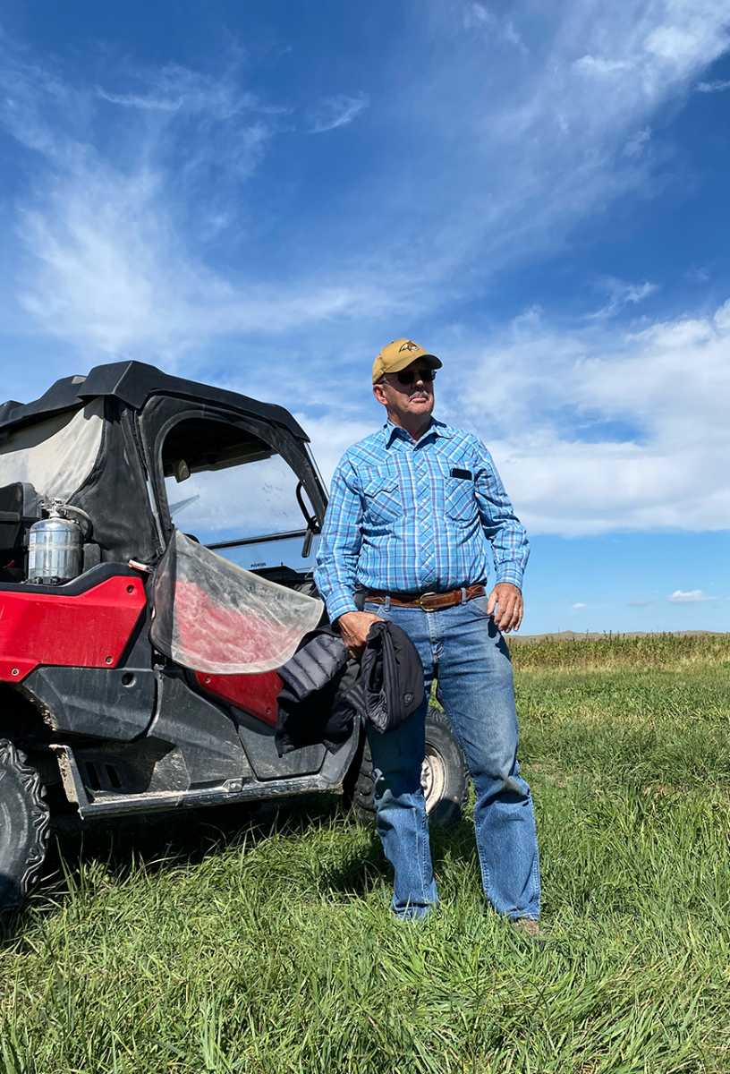 Mark Kossler stands in front of his ATV in a green field, looking out on his sustainable agriculture operation.